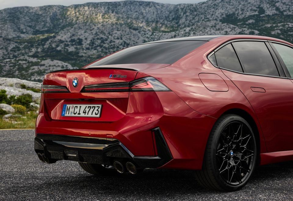 A red BMW M3 50 sedan seen from the rear quarter, parked on a road with mountains in the background
