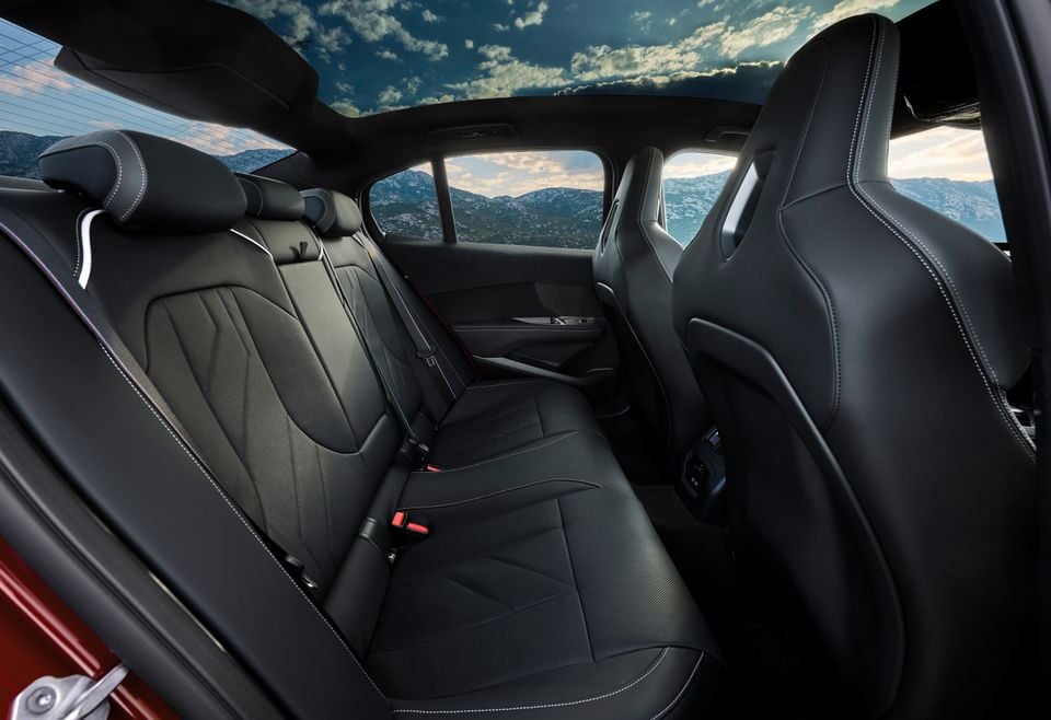 The black leather rear seats of a 2027 BMW M350 xDrive, viewed from behind with a panoramic sunroof and mountain scenery visible through the windows.