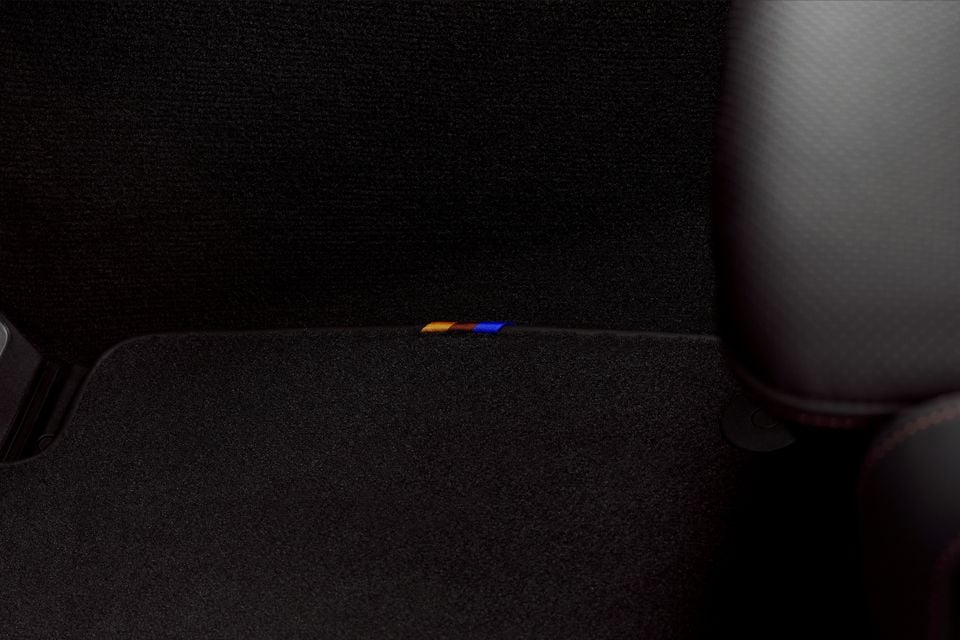 Close-up of a BMW X3 M50 interior showing M-colour stitching detail on the dark carpeted boot trim