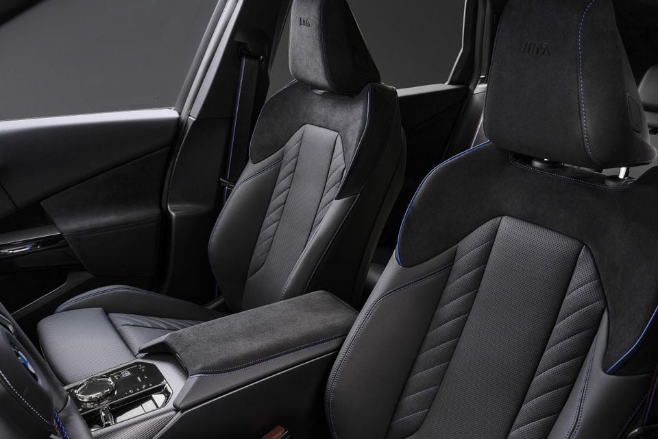 Black leather and suede front seats with blue stitching inside a 2027 BMW X3 M50, showing M badging on the headrests and centre console.