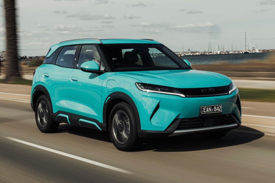 A turquoise BYD Atto 2 SUV driving along a coastal road near a marina.