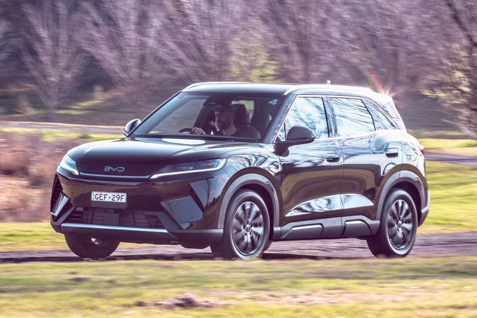 A black BYD Atto 2 SUV driven along a road, seen from the front quarter with the driver visible inside
