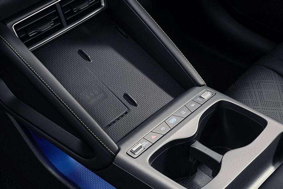 Close-up of the centre console in a car showing a wireless phone charging pad, storage tray, cup holders and control buttons including start/stop and hazard lights.