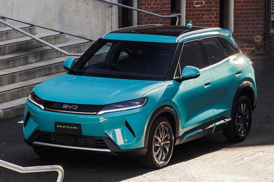 A teal BYD Atto 2 DM-i SUV parked outside a brick building, viewed from the front quarter angle