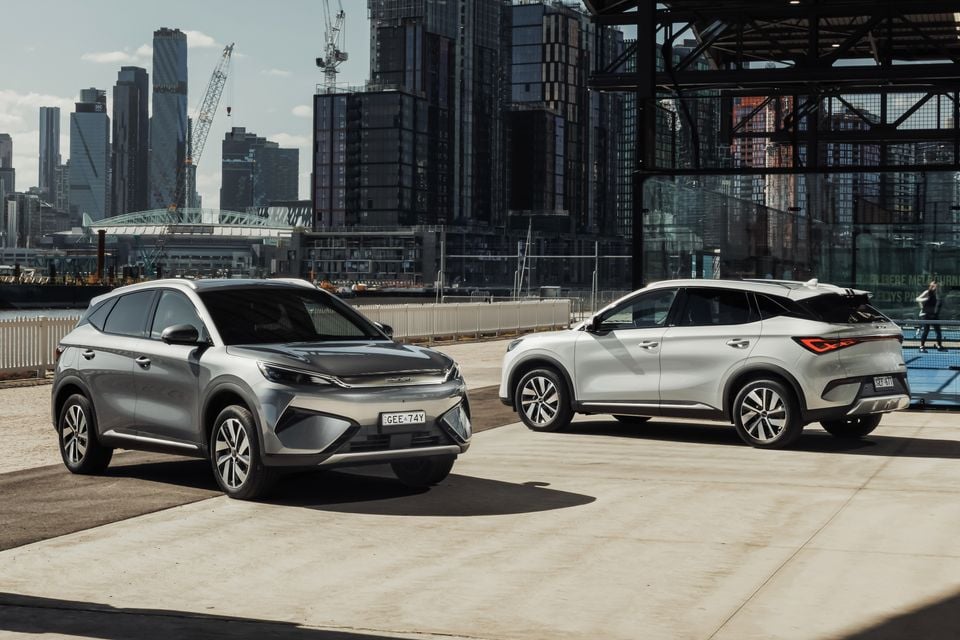 Two 2027 BYD Atto 3 Evo SUVs, one silver and one white, parked facing opposite directions with a city skyline in the background.