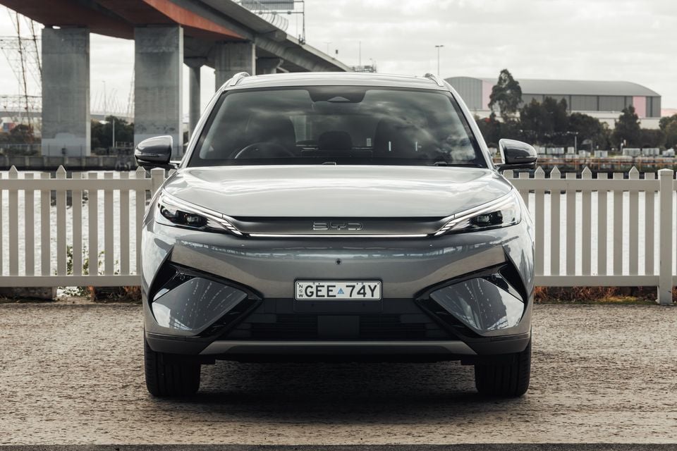 A grey BYD Atto 3 SUV parked facing the camera near a waterfront with a bridge in the background.