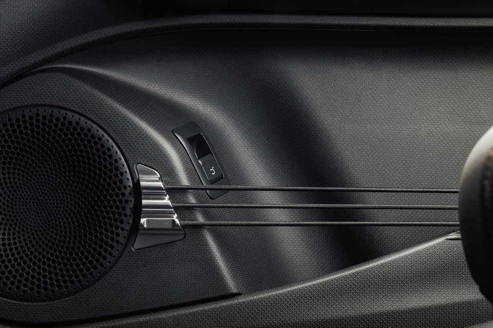 Close-up of a car door panel showing a speaker grille, mirror adjustment switch, and window control on a 2027 BYD Atto 3 Evo