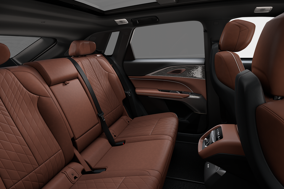 Interior rear seating of a 2027 Cadillac Lyriq showing quilted brown leather seats, seatbelts, door trim with speaker, and rear passenger controls