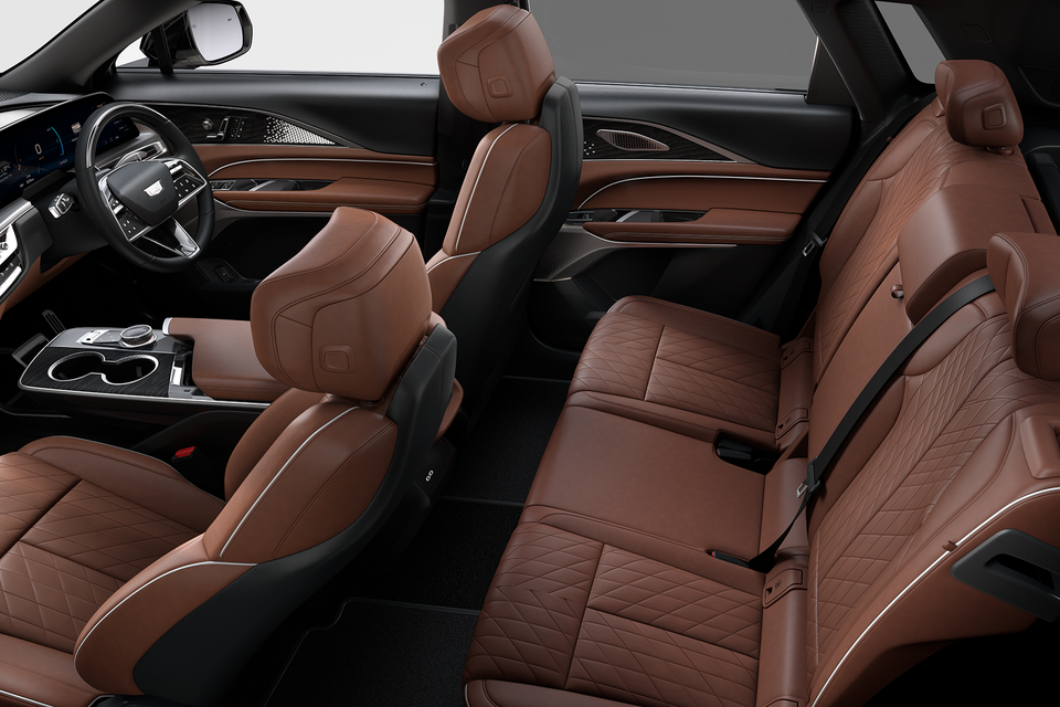 Interior of a 2027 Cadillac Lyriq showing tan brown quilted leather seats across all rows, with the Cadillac steering wheel and centre console visible from a side-on view