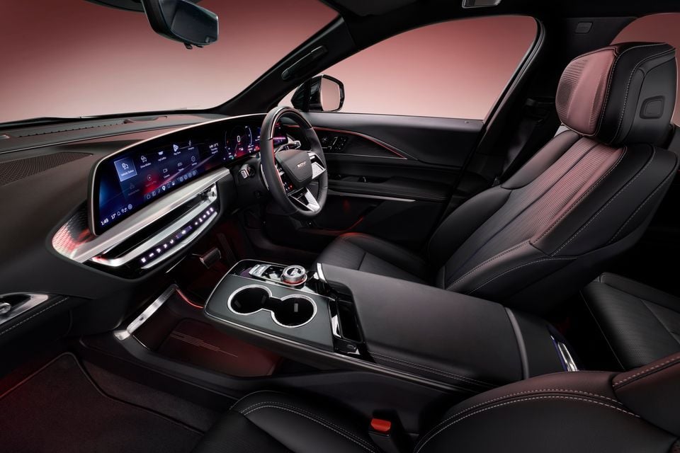 Interior of a 2027 Cadillac LYRIQ-V showing the panoramic display screen, centre console, steering wheel, and dark leather seats with burgundy accents
