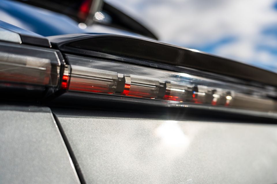 Close-up of the tail light on a silver 2027 Cadillac Lyriq V, showing its distinctive LED light bar design against a cloudy sky.