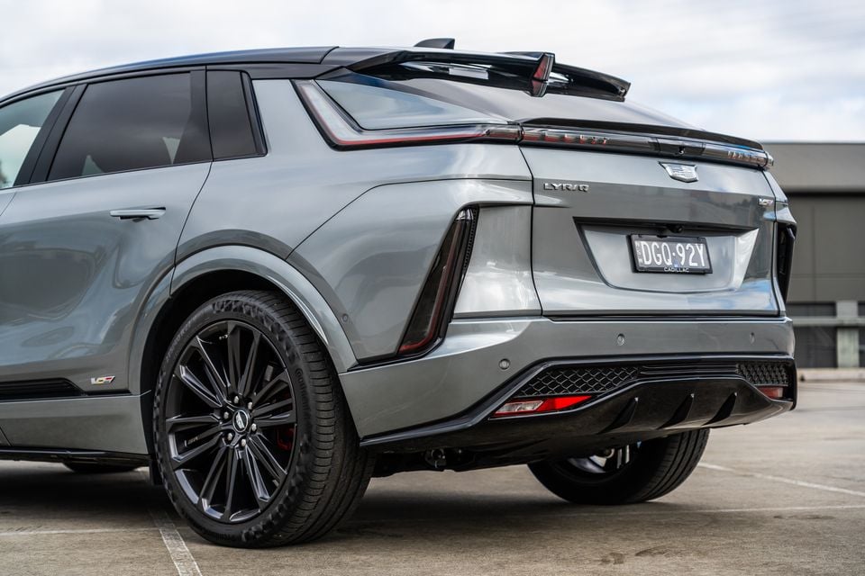 Rear three-quarter view of a grey 2027 Cadillac LYRIQ-V SUV parked in a car park, showing the tailgate badging, LED tail-lights, rear diffuser and black alloy wheels