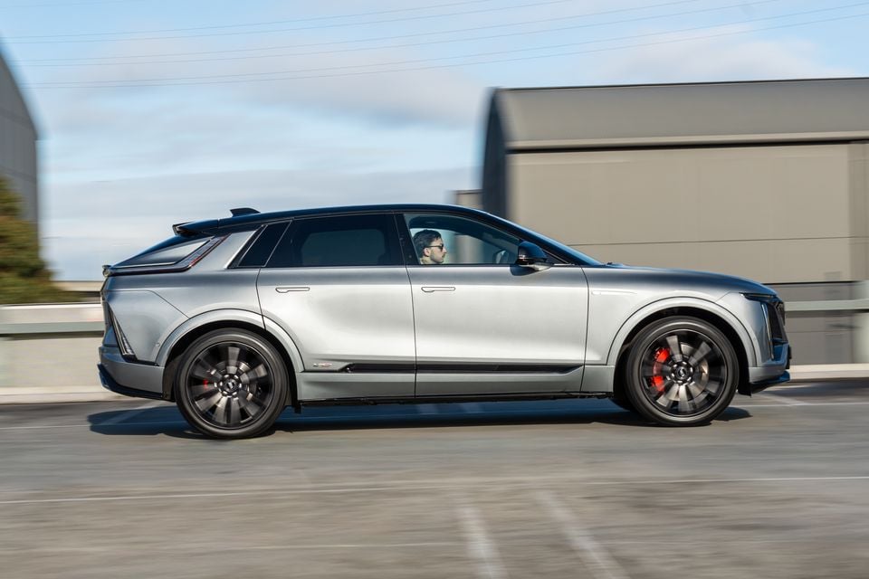 A silver Cadillac Lyriq V SUV seen from the side while driving on a road