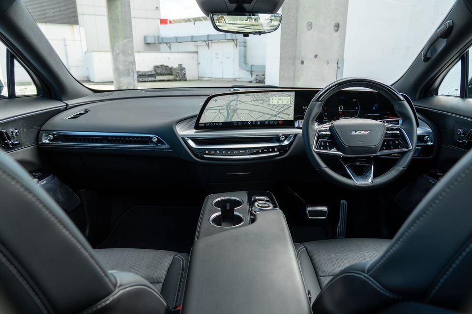 Interior of a Cadillac Lyriq V showing the dashboard, large central infotainment touchscreen displaying navigation, digital instrument cluster, steering wheel, and centre console