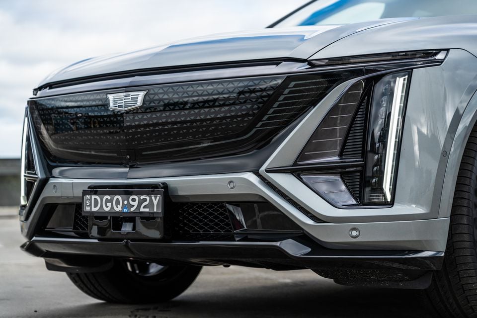 Close-up of the front grille and headlight of a silver 2027 Cadillac Lyriq SUV, showing the Cadillac badge and angular LED lighting details.
