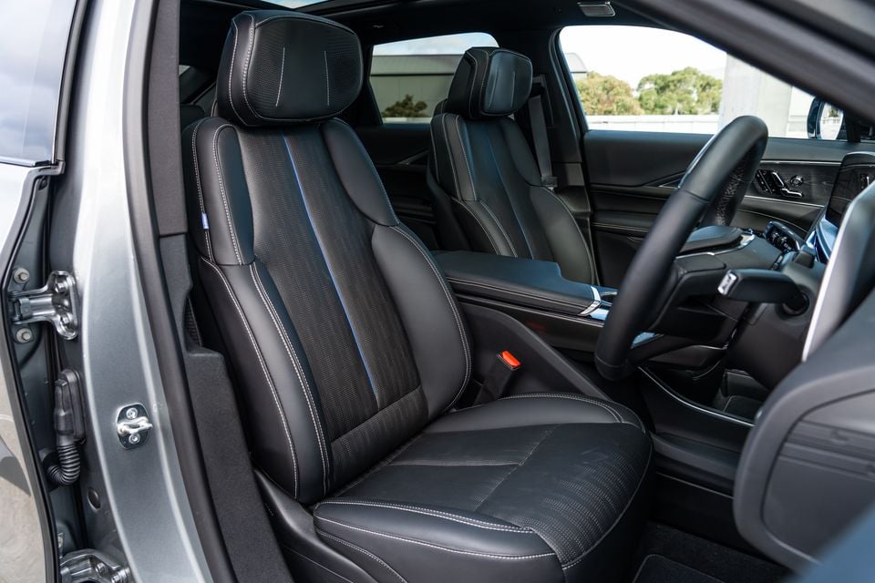 Black leather front seats of a 2027 Cadillac Lyriq, viewed from the driver's side door opening, showing contrast stitching and blue accent piping with the steering wheel and dashboard visible in the background