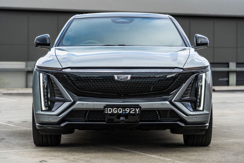 Front view of a grey 2027 Cadillac LYRIQ SUV parked in a car park, showing its bold grille, angular LED headlights and NSW number plate