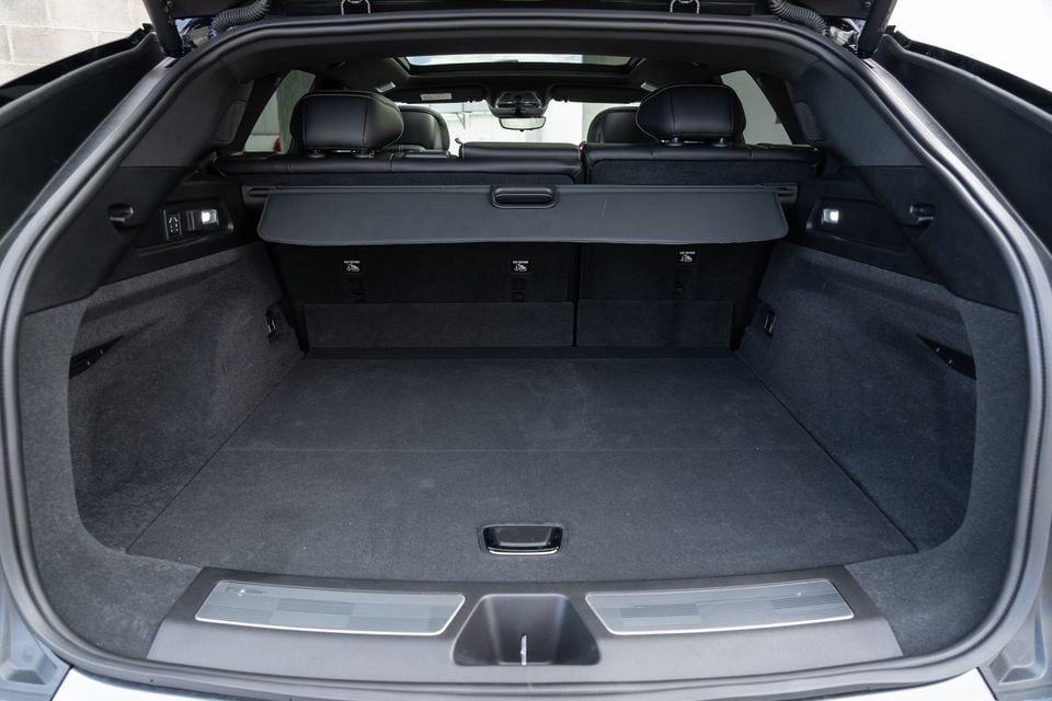 The open boot of a 2027 Cadillac Lyriq showing a large carpeted cargo area with a retractable cargo cover and top-tether anchor points visible at the rear seat backs.