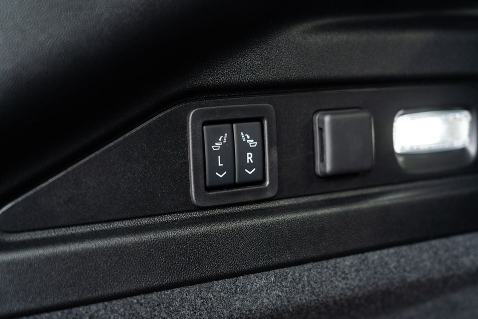 Close-up of rear seat fold-down controls on the interior trim panel of a Cadillac Lyriq, showing left and right split-seat buttons alongside window and door handle controls.