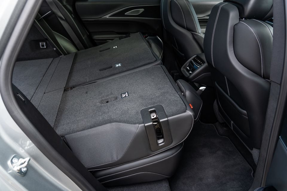 Interior of a 2027 Cadillac LYRIQ showing the rear seats folded flat to expand the boot space, with black leather upholstery and white contrast stitching visible on the front seat