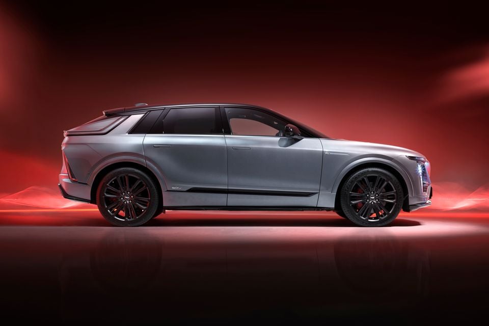 A silver 2027 Cadillac Lyriq-V SUV photographed from the side in a dramatic red-lit studio setting