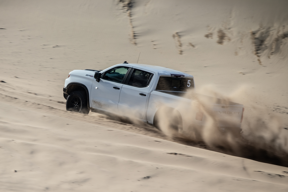 A white Chevrolet Silverado ZR2 ute driving through sand dunes, kicking up a large dust cloud from the rear