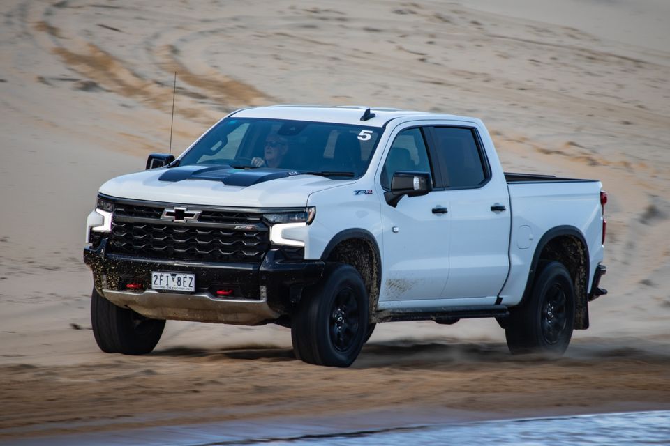 A white Chevrolet Silverado ZR2 ute driving on a sandy beach, seen from the front-side