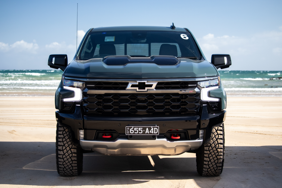 A black Chevrolet Silverado ZR2 ute seen from the front, parked on a beach with the ocean in the background