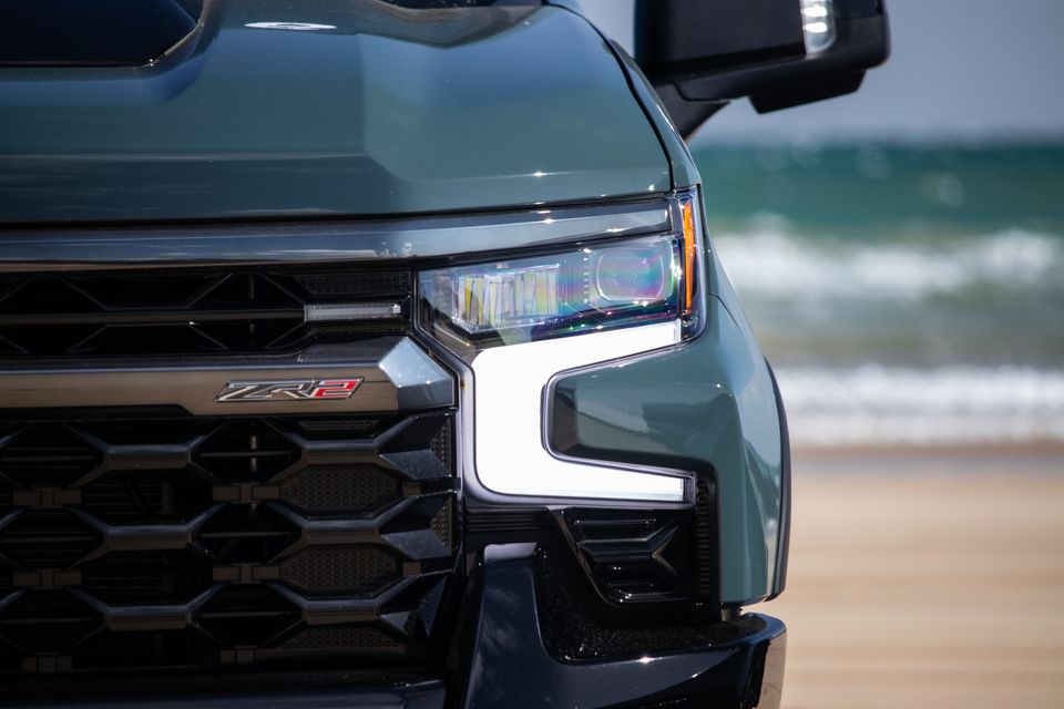 Close-up of the front grille and LED headlight of a green Chevrolet Silverado ZR2, photographed on a beach
