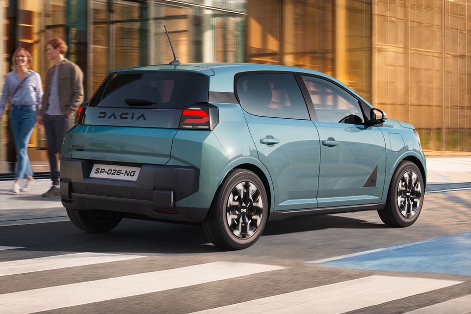 A light blue Dacia Spring hatchback seen from the rear three-quarter angle on a city street