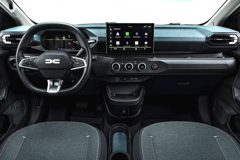 Interior of a Dacia Spring showing the dashboard, steering wheel, central touchscreen infotainment system with Android Auto and Apple CarPlay, climate controls, and front seats