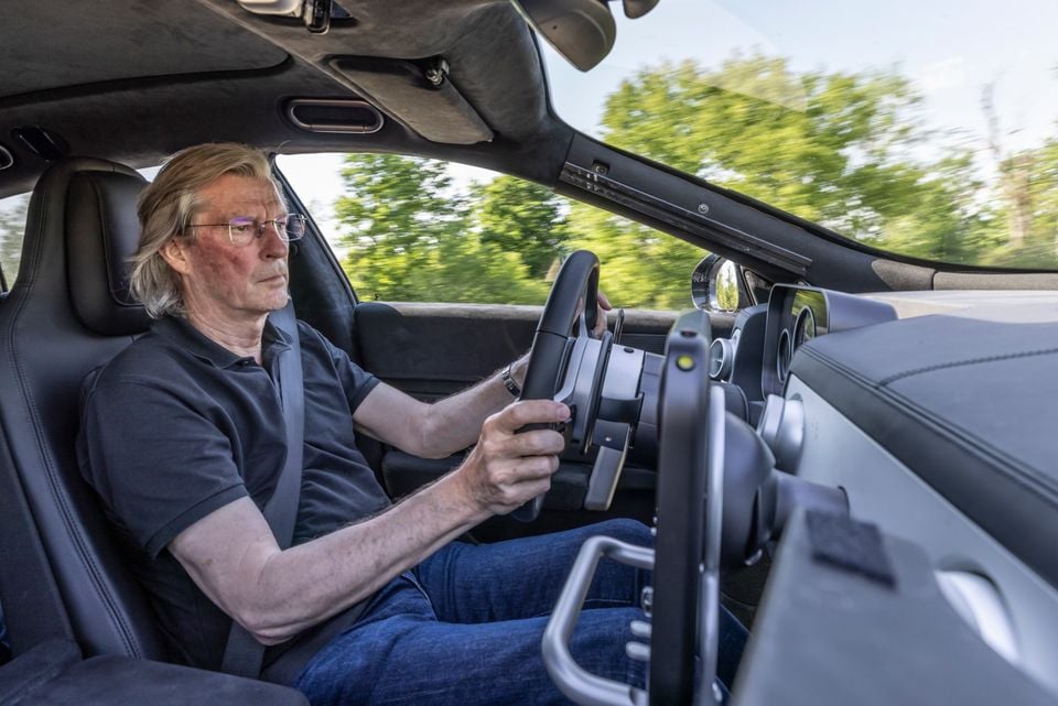 A man driving a sports car interior, gripping the steering wheel while in motion on a tree-lined road