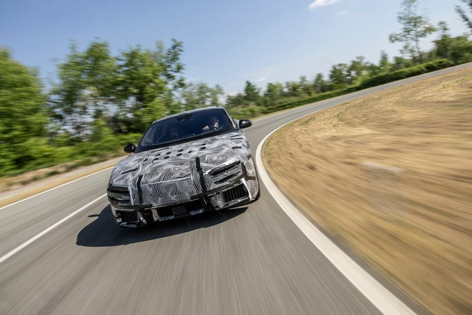 A camouflaged Ferrari Luce prototype sedan driving at speed on a test track, seen from the front