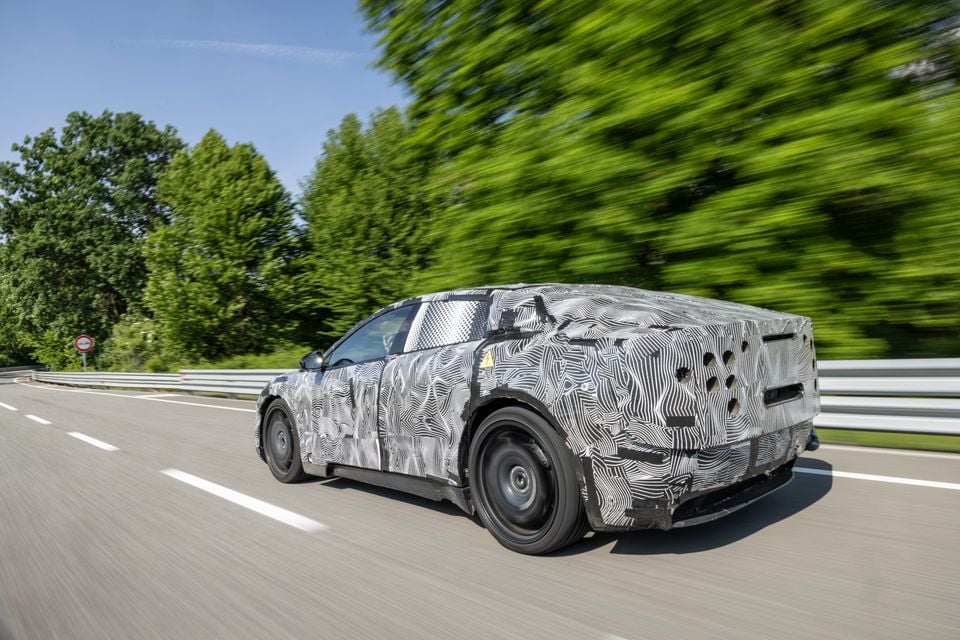 A camouflaged 2027 Ferrari Luce prototype coupe seen from the rear-side while driving on a road