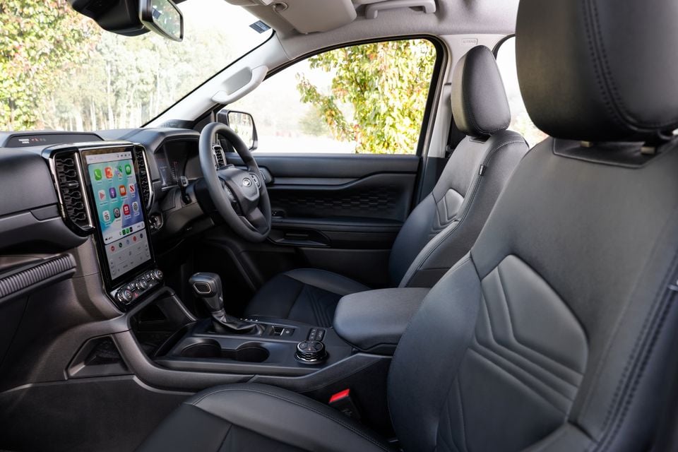 Interior of a Ford Everest showing the front cabin with large portrait touchscreen infotainment display running Apple CarPlay, leather seats, centre console, and steering wheel, shot from the passenger side in right-hand drive configuration
