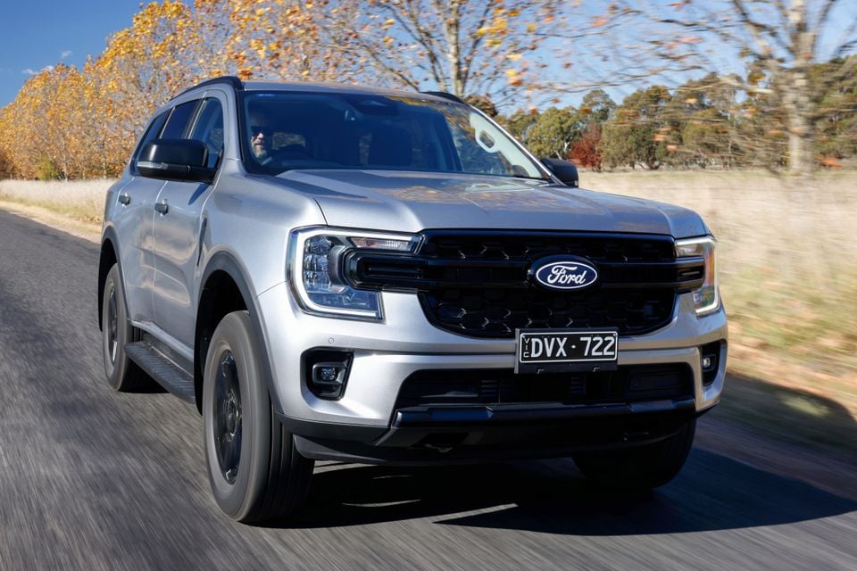 A silver Ford Everest large SUV driving on a country road, seen from the front and side