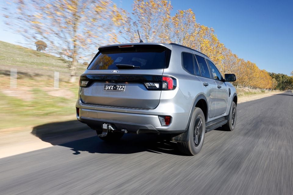A silver Ford Everest SUV seen from the rear while driving on a country road, fitted with a tow bar