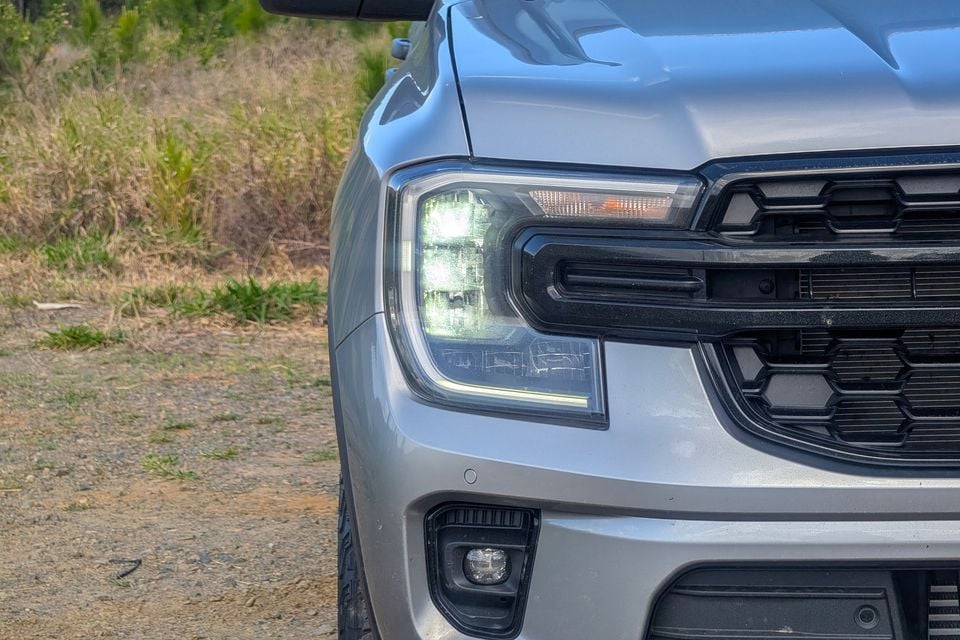 Close-up of the headlight and front grille on a silver Ford Everest Active ute, photographed outdoors on a gravel surface.
