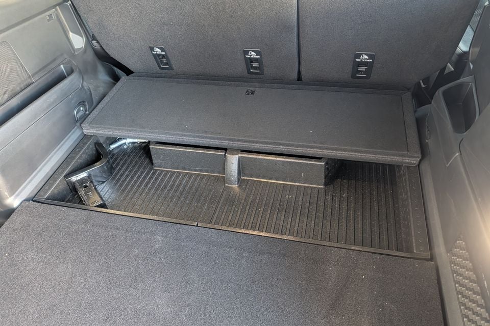 The boot area of a Ford Everest showing an under-floor storage compartment with a lift-up panel, revealing a recessed tray beneath, with three top-tether anchor points visible on the rear seat backs.