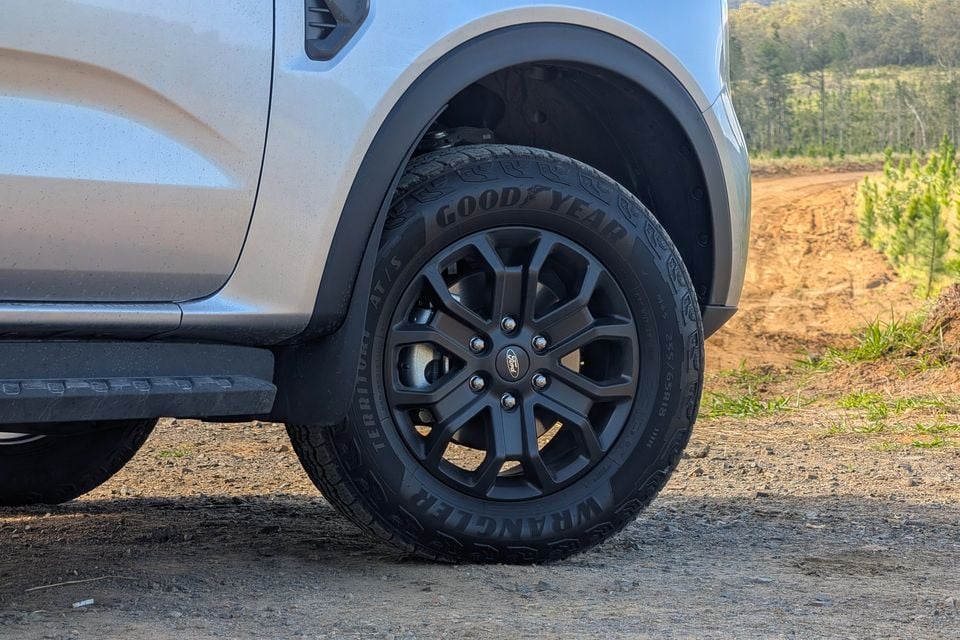 Close-up of a black multi-spoke alloy wheel fitted with a Goodyear Wrangler Territory AT/S tyre on a white Ford Everest Active, parked on a dirt track
