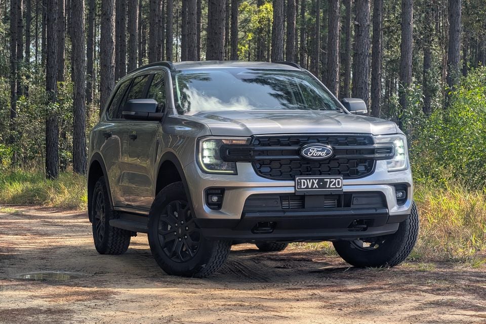A silver Ford Everest SUV parked on a dirt track surrounded by pine trees, seen from the front