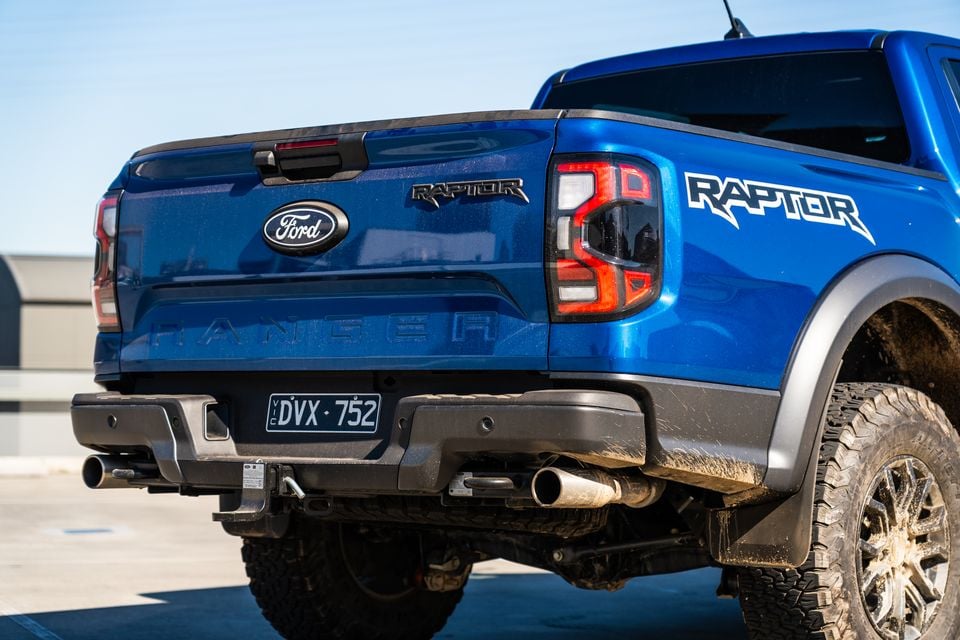 A blue Ford Ranger Raptor dual-cab ute, seen from the rear quarter with focus on its taillight, badge and dual exhaust.