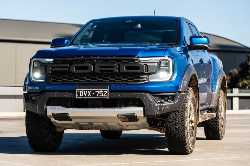 A blue Ford Ranger Raptor ute photographed from a low angle at the front, showing its off-road tyres and grille