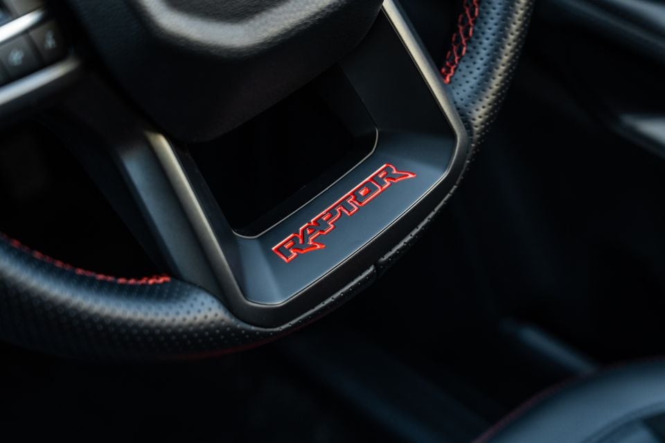 Close-up of the "Raptor" badge on the steering wheel of a Ford Ranger Raptor, with red stitching on black leather