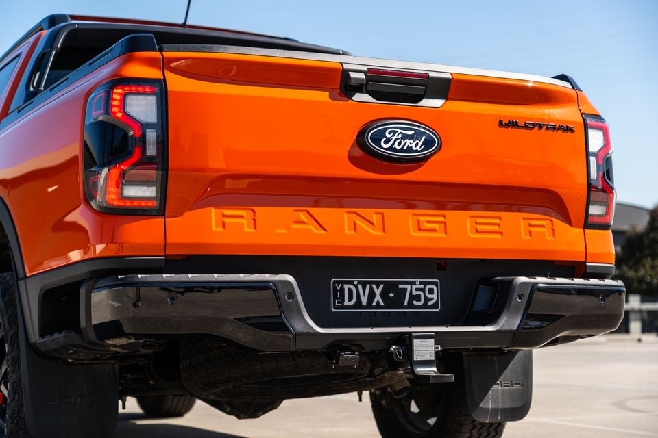 Rear view of an orange Ford Ranger Wildtrak ute showing the tailgate, LED tail lights, and tow bar, with a Victorian number plate