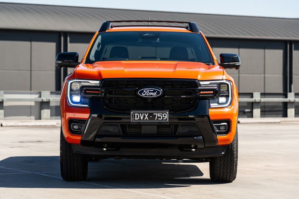 Orange Ford Ranger Wildtrak ute seen from the front, showing its black grille, LED headlights and Victorian number plate, parked on an open hardstand