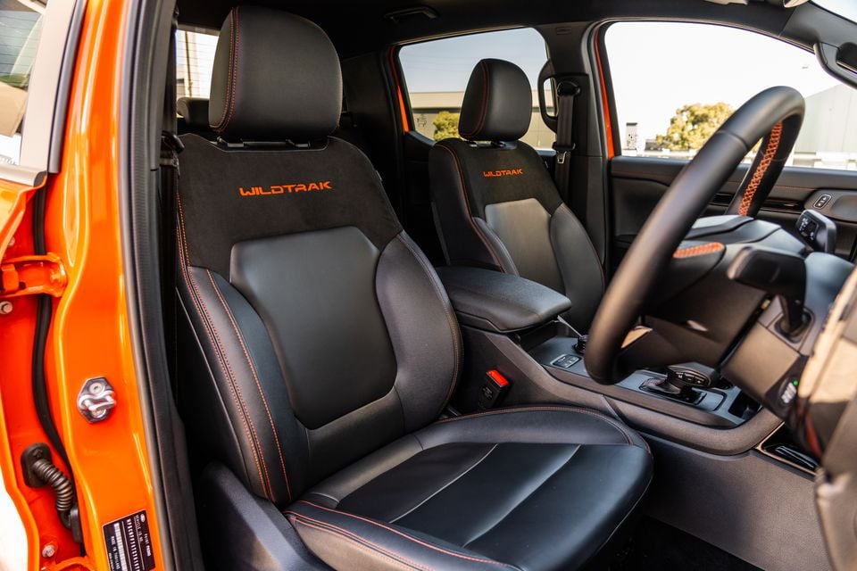 Ford Ranger Wildtrak front interior showing black seats with orange Wildtrak branding and orange contrast stitching, alongside the steering wheel and centre console