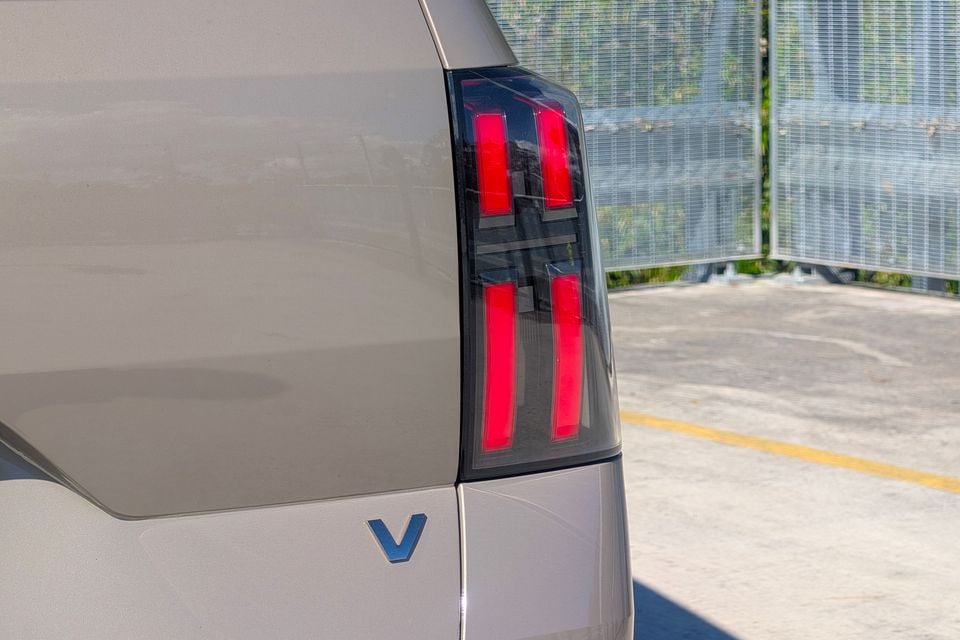 Close-up of the rear tail light and badge on a GAC Aion V, showing distinctive red LED light elements and a blue V emblem on the silver bodywork.