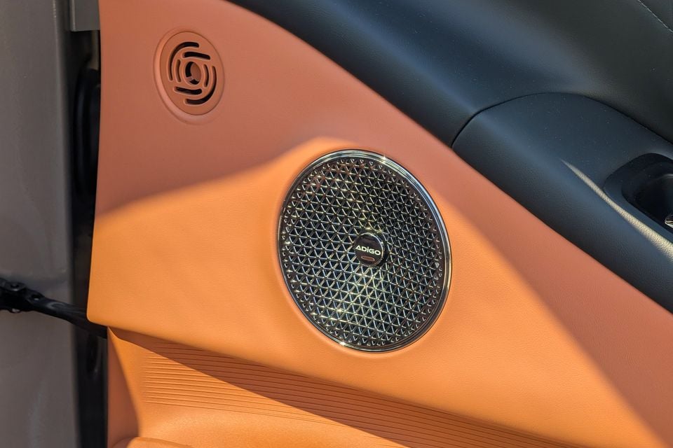 An ADiGo branded door speaker with a chrome surround set into an orange leather door panel inside the GAC Aion V