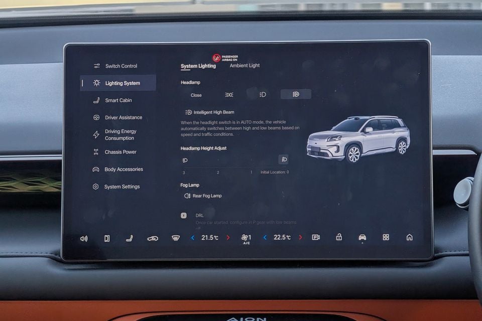 The infotainment touchscreen of a GAC Aion V displaying the Lighting System settings menu, including headlamp, headlamp height adjust, fog lamp and DRL options.